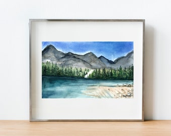 Pode incluir: Uma pintura a aquarela emoldurada de uma cena de lago de montanha. A pintura representa um lago com uma costa arenosa em primeiro plano, uma linha de árvores perenes no meio e uma cordilheira de montanhas azul escuro no fundo. O céu é azul brilhante com algumas nuvolens brancas.