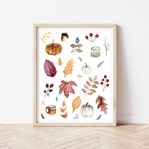 Pode incluir: Uma impressão de aquarela com uma variedade de elementos outonais, incluindo abóboras, folhas, bagas, bolotas e uma vela. A impressão está em uma moldura marrom clara e tem um fundo branco.