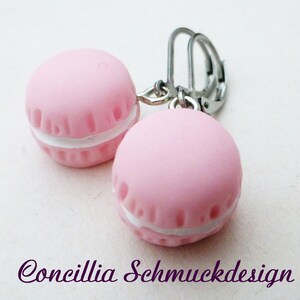 Könnte beinhalten: Ein Paar rosa Macaron-Ohrringe mit weißer Füllung und silberfarbenen Klappbügelverschlüssen. Die Ohrringe sind hellrosa und haben eine strukturierte Oberfläche. Der Text "Concillia Schmuckdesign" befindet sich am unteren Bildrand.