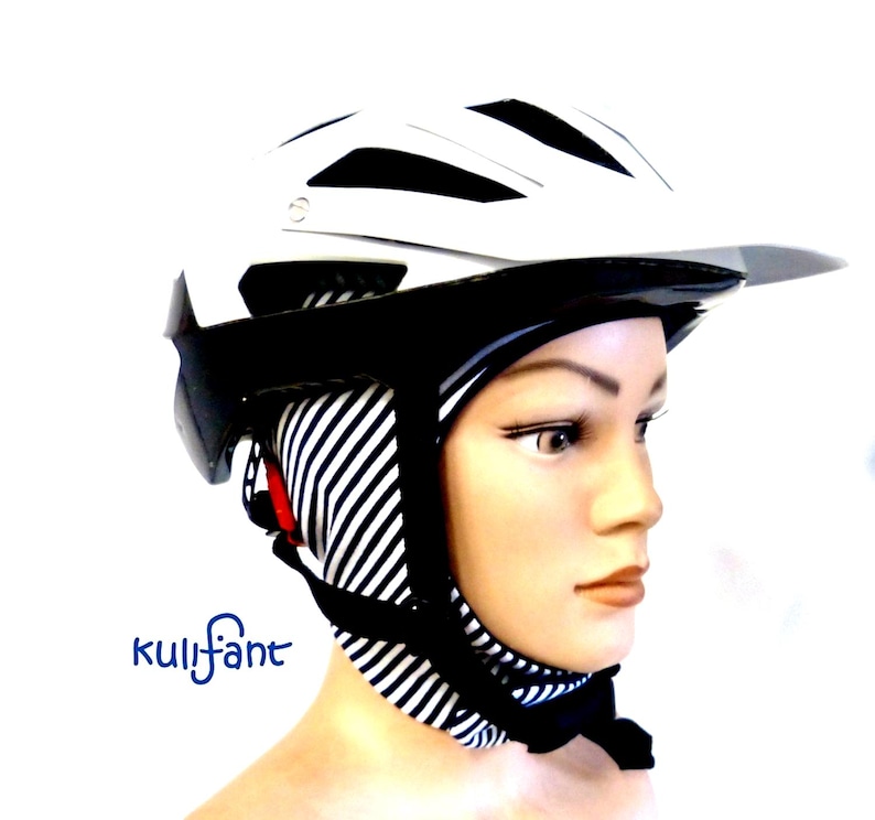 May include: A white and black bicycle helmet worn over a black and white striped fabric head covering. The helmet features a visor and ventilation slots. The text Kulifant is printed in blue on the lower left side of the image.