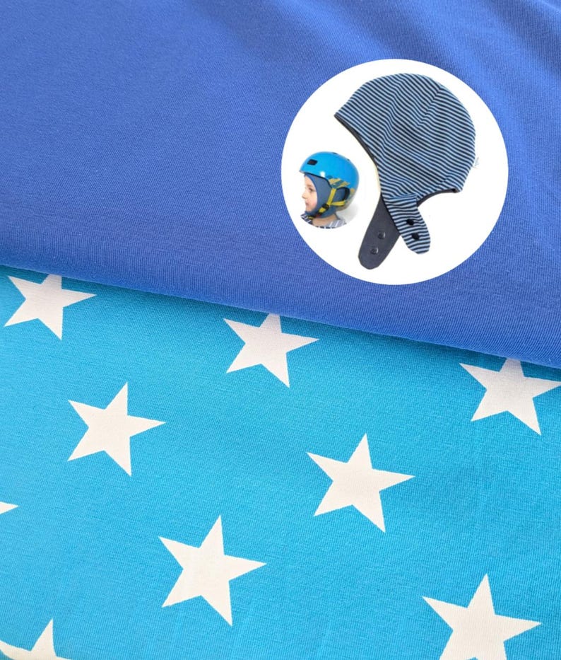 May include: A blue fabric layer sits atop a bright blue fabric featuring a white star pattern. A circular inset shows a blue and black striped hat with ear flaps and snap closures, alongside a blue helmet worn by a child with yellow straps.