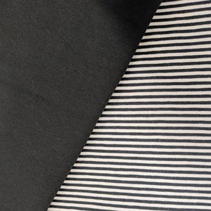 May include: A textile fabric featuring two distinct sections. One side consists of a solid, matte black fabric. The adjacent side displays a pattern of thin, horizontal black and white stripes, creating a high-contrast visual texture across the surface.