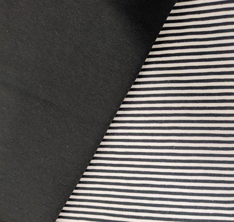 May include: A textile fabric featuring two distinct sections. One side consists of a solid, matte black fabric. The adjacent side displays a pattern of thin, horizontal black and white stripes, creating a high-contrast visual texture across the surface.