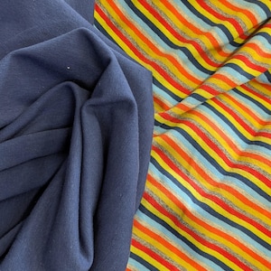 May include: A solid dark navy blue fabric folded next to a multi-coloured striped fabric. The striped fabric features repeating horizontal lines in shades of bright orange, yellow, light blue, and dark navy blue against a heather grey background.