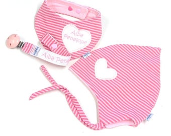 May include: A baby gift set with a pink and white striped bib, pacifier clip, and bonnet. The bib and bonnet have white heart appliqués. The pacifier clip and bib are embroidered with the name "Alba Penelope".