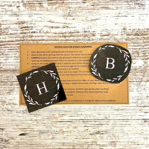 May include: Two black and white stencils with a wreath design and the letters "H" and "B" in white. The stencils are on a brown background with instructions for stencil placement.