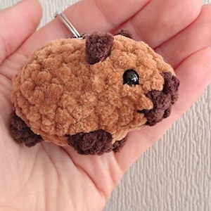 May include: A brown and black crocheted plush keychain shaped like a guinea pig. The keychain has a silver metal ring.