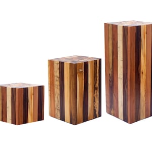 Puede incluir: Tres expositores de madera de diferentes tamaños, cada uno hecho de múltiples tablas de madera en diferentes tonos de marrón, beige y rojo.