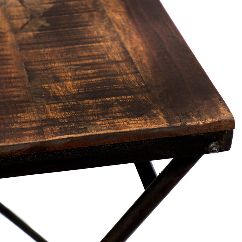 Peut inclure: Gros plan sur une table en bois rustique avec une finition marron fonc&eacute;. Le plateau a un aspect vieilli avec le grain du bois visible et un cadre en m&eacute;tal noir. Les pieds de la table sont inclin&eacute;s et en m&eacute;tal fonc&eacute;.