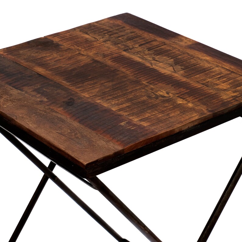 Peut inclure: Petite table d'appoint carr&eacute;e avec un plateau en bois brun fonc&eacute; vieilli et une structure en m&eacute;tal noir. Le plateau semble &ecirc;tre en bois r&eacute;cup&eacute;r&eacute;, avec un grain et une texture visibles. Les pieds sont crois&eacute;s pour la stabilit&eacute;.