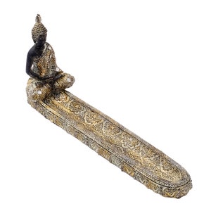 Könnte beinhalten: Ein dekorativer Räucherstäbchenhalter mit einer sitzenden Buddha-Figur. Der Buddha ist dunkel gefärbt mit goldenen Akzenten und sitzt auf einer detaillierten, länglichen Ablage. Die Ablage hat ein verziertes, goldfarbenes Muster.