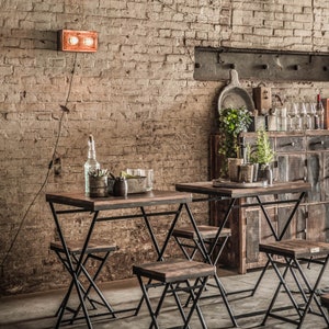 Peut inclure: Deux petites tables en bois fonc&eacute; avec des pieds en m&eacute;tal noir et des tabourets assortis sont install&eacute;es devant un mur de briques. Un luminaire cuivr&eacute; est mont&eacute; sur le mur. La sc&egrave;ne sugg&egrave;re un cadre de bar ou de caf&eacute; rustique.