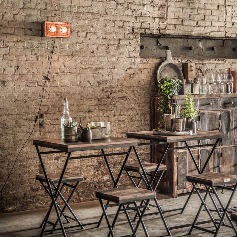 Peut inclure: Deux petites tables en bois fonc&eacute; avec des pieds en m&eacute;tal noir et des tabourets assortis sont install&eacute;es devant un mur de briques. Un luminaire cuivr&eacute; est mont&eacute; sur le mur. La sc&egrave;ne sugg&egrave;re un cadre de bar ou de caf&eacute; rustique.
