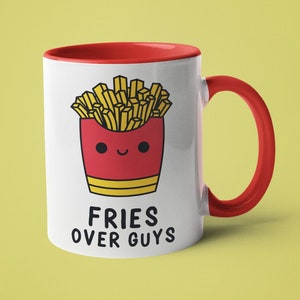 May include: White ceramic mug with a red interior and handle. The mug features a cartoon illustration of a red french fry container with a smiling face and golden fries. The text "FRIES OVER GUYS" is printed below the illustration.