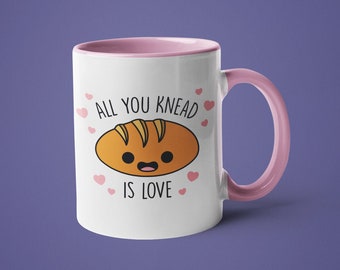 Könnte beinhalten: Weiße Keramiktasse mit rosafarbenem Rand und Henkel. Die Tasse hat ein Cartoon-Brot-Design mit dem Text "Alles, was du brauchst, ist Liebe".