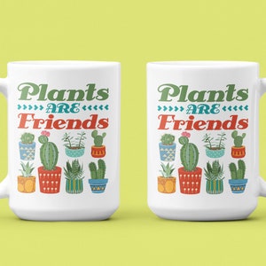 May include: Two white ceramic mugs with a green, red, and blue design of potted plants and the text "Plants are Friends".
