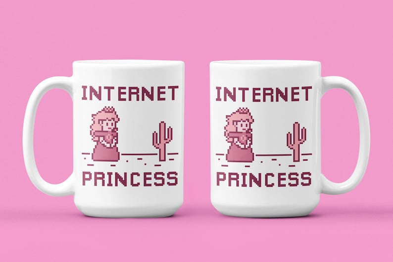 K&ouml;nnte beinhalten: Wei&szlig;e Keramiktasse mit dem Text "INTERNET PRINCESS" in einer pixeligen Schriftart, zusammen mit einem pixeligen Bild einer Prinzessin und eines Kaktus. Die Tasse hat einen Henkel und steht vor einem rosa Hintergrund.