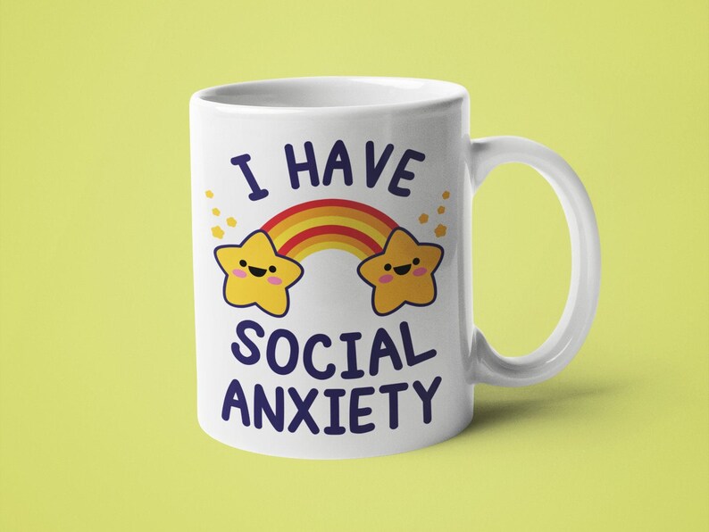 May include: White ceramic mug with a rainbow and two yellow stars with faces. The text "I have social anxiety" is printed on the mug.
