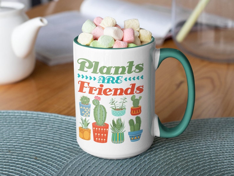 May include: White ceramic mug with a green handle. The mug has a colorful design of potted cacti and the text "Plants are Friends".