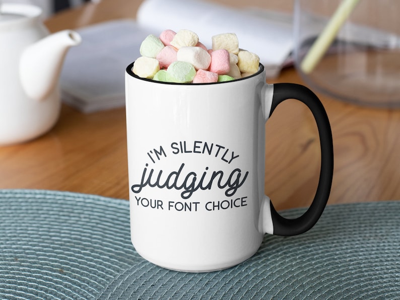 Puede incluir: Taza de cer&aacute;mica blanca con asa y borde negros. La taza tiene un gr&aacute;fico negro que dice "Estoy juzgando silenciosamente tu elecci&oacute;n de fuente".