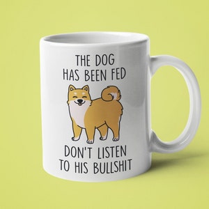 May include: White ceramic mug with a cartoon Shiba Inu dog and the text "The dog has been fed don't listen to his bullshit".