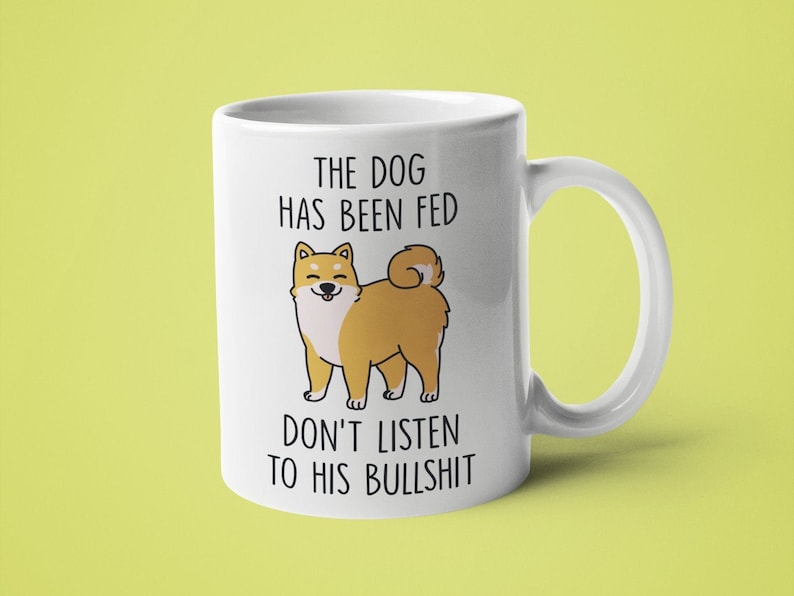 May include: White ceramic mug with a cartoon Shiba Inu dog and the text "The dog has been fed don't listen to his bullshit".