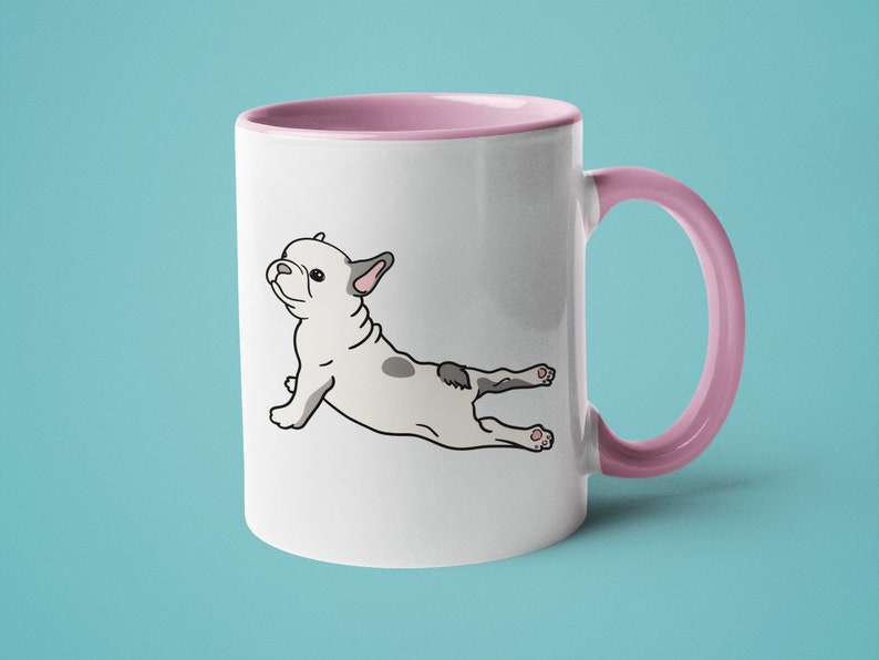 May include: White ceramic mug with a pink rim and handle. The mug features a cartoon illustration of a French bulldog doing yoga.