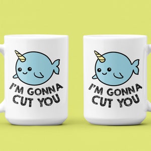 May include: Two white ceramic mugs with a cartoon narwhal design. The narwhal is light blue with a yellow horn and the text "I'm gonna cut you" in black.