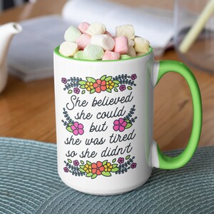 May include: White ceramic mug with a green handle. The mug has a floral design and the text "She believed she could but she was tired so she didn't".