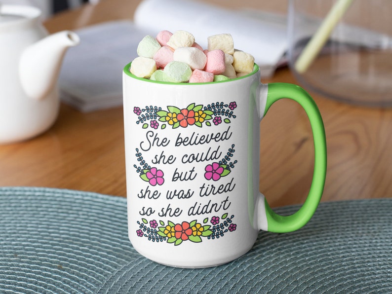 May include: White ceramic mug with a green handle. The mug has a floral design and the text "She believed she could but she was tired so she didn't".