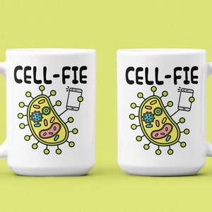 May include: Two white ceramic mugs with a black outline of a cell phone taking a selfie with a cartoon cell. The text "CELL-FIE" is printed in black on each mug.