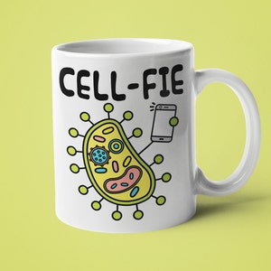May include: White ceramic mug featuring a black and white illustration of a cell taking a selfie with a smartphone. The text "CELL-FIE" is printed on the mug.