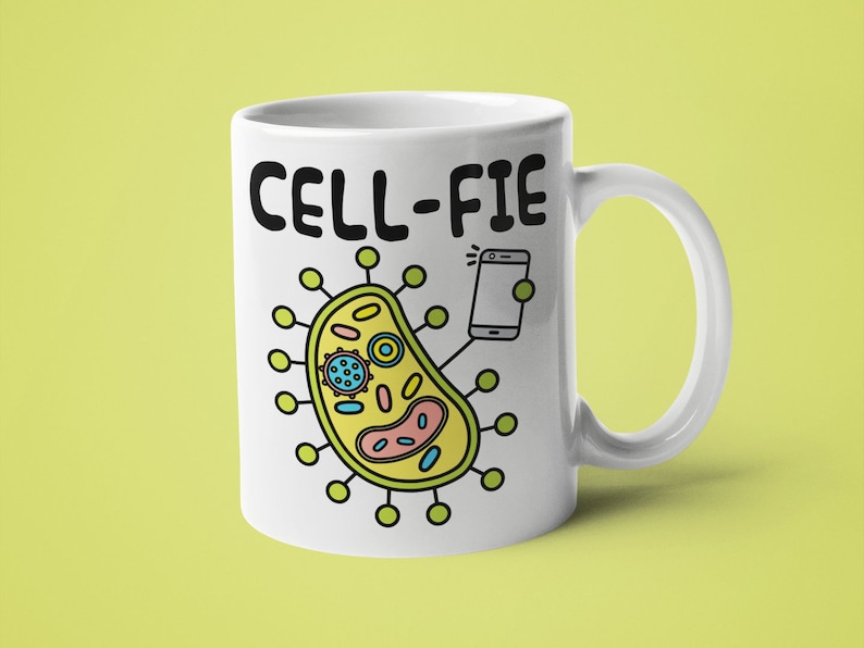 May include: White ceramic mug featuring a black and white illustration of a cell taking a selfie with a smartphone. The text "CELL-FIE" is printed on the mug.