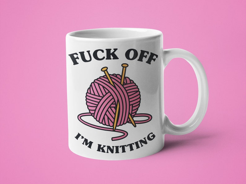 K&ouml;nnte beinhalten: Wei&szlig;e Keramiktasse mit einem schwarzen und rosa Motiv. Das Motiv sagt "F*ck Off I'm Knitting" und zeigt eine rosa Wollkn&auml;uel mit zwei Stricknadeln.