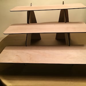 Puede incluir: Un expositor de madera de tres niveles con un acabado de madera natural. Cada nivel es rectangular y tiene un borde negro. El expositor est&aacute; hecho de madera contrachapada y es perfecto para exhibir art&iacute;culos peque&ntilde;os.