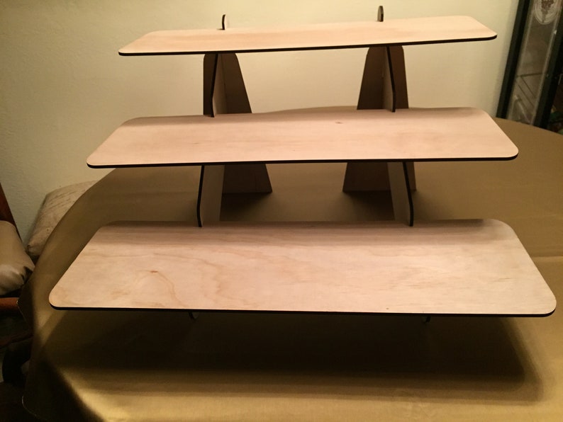 Puede incluir: Un expositor de madera de tres niveles con un acabado de madera natural. Cada nivel es rectangular y tiene un borde negro. El expositor est&aacute; hecho de madera contrachapada y es perfecto para exhibir art&iacute;culos peque&ntilde;os.