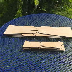Puede incluir: Dos juegos de piezas de madera, probablemente para un proyecto artesanal, se colocan sobre una mesa de metal azul. El juego m&aacute;s grande tiene cinco piezas, mientras que el juego m&aacute;s peque&ntilde;o tiene cuatro piezas.