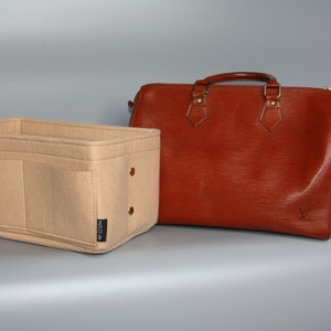 May include: Beige felt bag organizer with multiple compartments and a black label that says "net27.de". The organizer is next to a brown leather handbag with gold hardware.