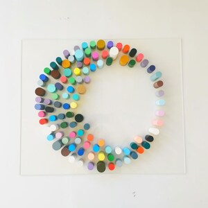 May include: A circular arrangement of colorful wooden cylinders on a clear acrylic surface. The cylinders are arranged in a spiral pattern, with the colors gradually changing from one end to the other.