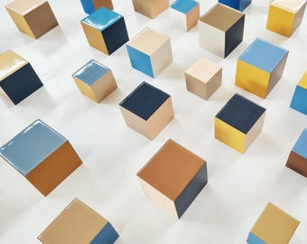May include: A collection of small, colorful, geometric blocks. Each block is painted in two colors, with one color on the top and another color on the bottom. The blocks are arranged in a grid pattern on a white surface.