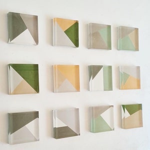 May include: A set of 12 square glass tiles with geometric patterns in shades of green, beige, and white.