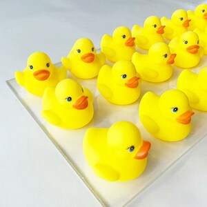 May include: A group of yellow rubber duck toys with orange beaks and black eyes. The ducks are arranged in a row on a white surface.