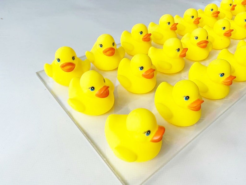 May include: A group of yellow rubber duck toys with orange beaks and black eyes. The ducks are arranged in a row on a white surface.