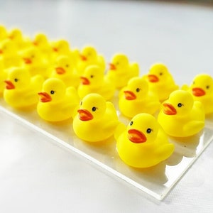 May include: A line of yellow rubber duck toys on a white surface. The ducks are arranged in a row, facing the same direction.