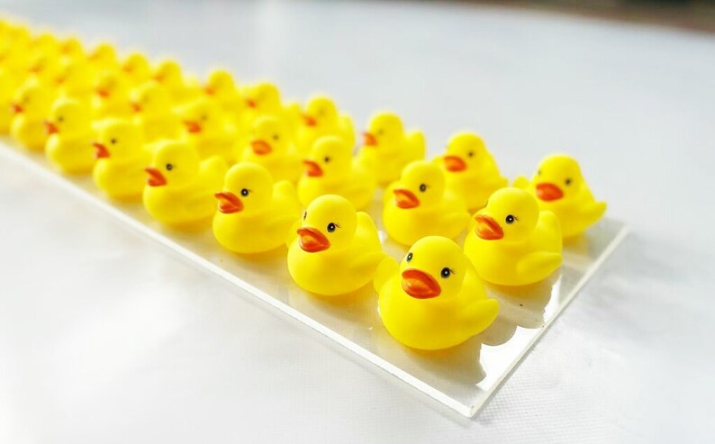 May include: A line of yellow rubber duck toys on a white surface. The ducks are arranged in a row, facing the same direction.