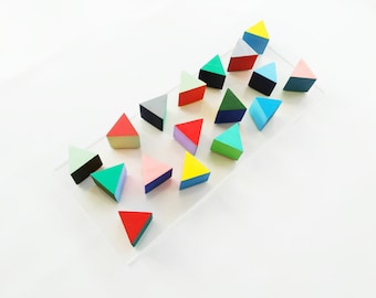 May include: A collection of colorful wooden triangle shapes arranged on a clear acrylic surface. The triangles are painted in various shades of red, green, blue, yellow, pink, and white.