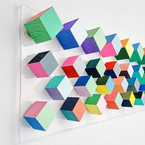 May include: A rectangular clear acrylic panel mounted with a grid of numerous small wooden cubes. Each cube features multiple sides painted in distinct, vibrant colors including neon pink, bright blue, lime green, orange, yellow, and deep purple.