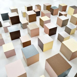 Op de afbeelding: Een verzameling van talrijke houten blokjes gerangschikt in een raster, elk geschilderd in een verscheidenheid aan gedempte aardetinten, waaronder tinten beige, bruin, tan, zachtroze, grijs en crème, met een gladde matte afwerking op alle zijden.