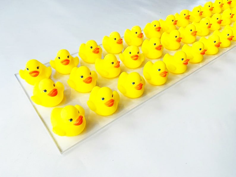 May include: A collection of yellow rubber duck toys arranged in a row on a clear surface. The ducks are all facing the same direction and have orange beaks and eyes.