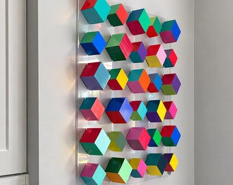 Può includere: Un oggetto da parete composto da una griglia di numerosi cubi tridimensionali in una varietà di colori vivaci tra cui rosso, blu, verde, giallo, arancione, viola e rosa, fissati su un pannello rettangolare in acrilico trasparente.
